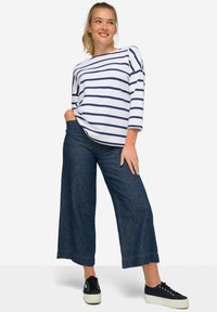 Vit och marinrandig båt-ringad topp med trekvartsärmar, parat med vida mörk denimjeans och svarta platåskor.