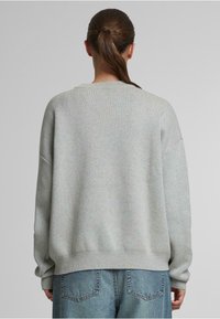 Suéter oversize gris claro con un tejido texturizado, puños y dobladillo acanalados. La vista posterior revela un amplio escote redondo. Combinado con denim claro.