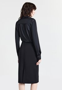 Schwarzes, langärmeliges Kleid mit einem satinähnlichen Oberteil und einem taillierten, strukturierten Rock. Verfügt über einen Schlitz im Rücken und Knopfmanschetten. Einfaches Design.