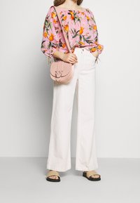 Donna che indossa un top rosa senza spalline con stampa di frutta arancione, pantaloni bianchi a gamba larga, sandali beige e una borsa a tracolla rosa.