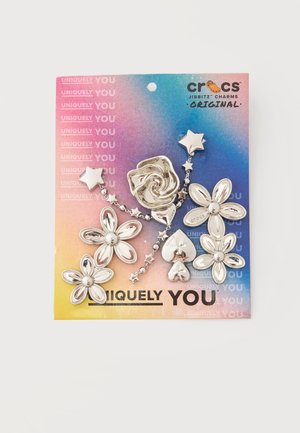 Sølv Crocs Jibbitz charms formet som blomster, stjerner, en rose og hjerter på en farverig gradientkort baggrund.