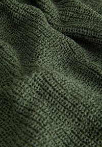 Tejido verde texturizado con un patrón de malla fina, que muestra una apariencia suave y de punto. El material parece ligero y transpirable.