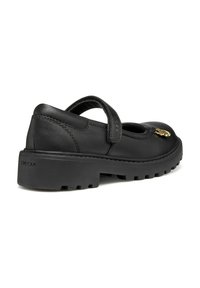 La chaussure Mary Jane en cuir noir présente une semelle en caoutchouc épaisse, une sangle réglable et un détail en métal doré à l'avant. Marquage Geox visible.
