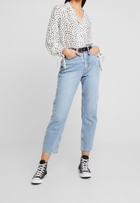 Camicia bianca con pois neri e polsini annodati. Jeans a vita alta azzurri chiaro con orli sfrangiati. Sneakers alte nere.