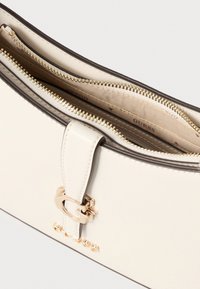 Crèmekleurige handtas van kunstleer met een sluiting en ritssluitingen in goudkleurig metaal en een gladde textuur. Subtiele branding zichtbaar aan de binnenkant.