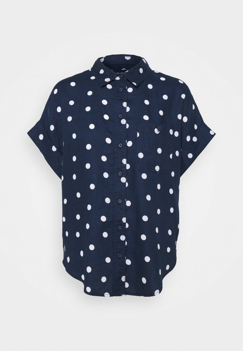 Chemise bleu marine à manches courtes avec boutons, à pois blancs et petite poche poitrine sur fond uni.