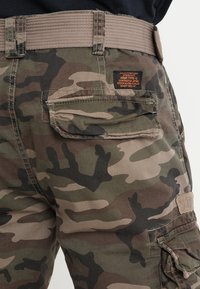 Camo cargo pants met een robuuste textuur. Kenmerken zijn een bruine stoffen riem, zijzakken en een geïntegreerd merklabel op de achterkant.
