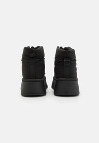 Svarte ankelstøvler med polstret overdel, elastisk snøring og tykk svart såle. Glatt tekstur med minimalistisk design.