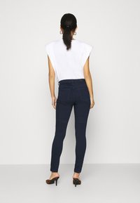 Mörkblå högmidjade jeans med smal passform, parat med en vit ärmlös topp med rund halsringning och lätt axelpaddning.