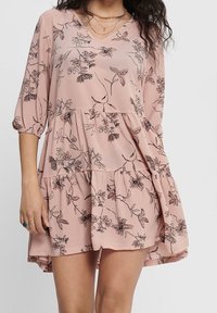 Robe à motif floral en tissu rose pâle, avec un décolleté en V, des manches trois-quarts et un ourlet en volants, offrant une coupe décontractée.