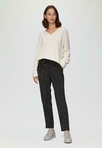 Witte, gebreide trui met een V-hals; zwarte, elastieken taillebroek met zakken; grijze sneakers met een dikke zool. Eenvoudig design en neutrale kleuren.