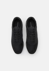Black athletic sneakers with a textured fabric upper, laces, and a padded collar. Features a contrasting white sole for grip.