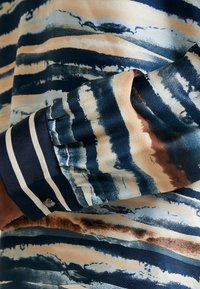 Mångfärgad blus med blå, beige och bruna abstrakta mönster. Mjuk tygkvalitet, knäppt manschett med randig detalj och en slät textur.