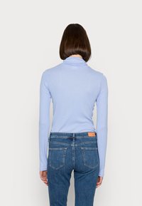 Camisola de manga longa azul claro com gola alta, combinada com jeans azul escuro com bolsos traseiros e um rótulo de couro na cintura.