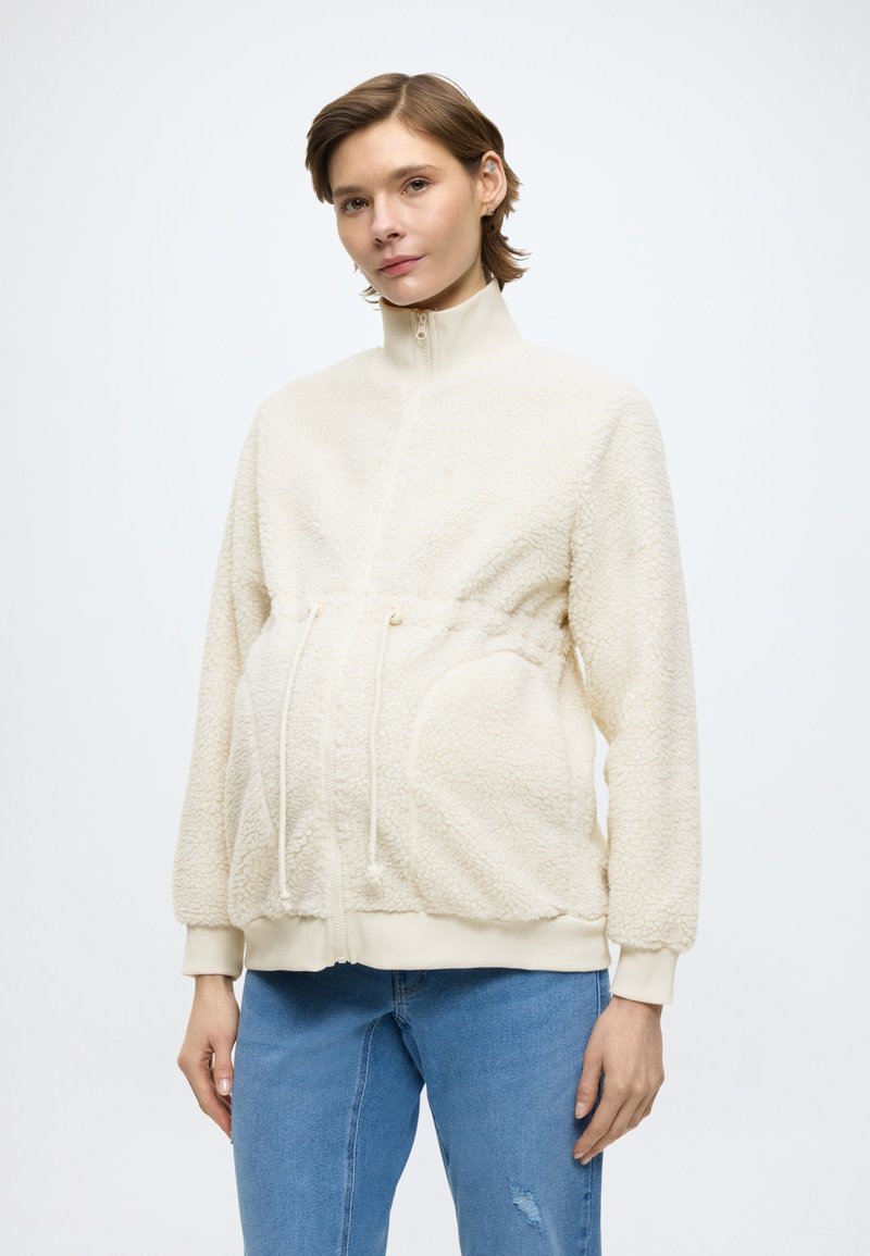 Giacca in pile color crema con collo alto, vita con coulisse e tasche laterali; presenta una superficie testurizzata e polsini a coste.