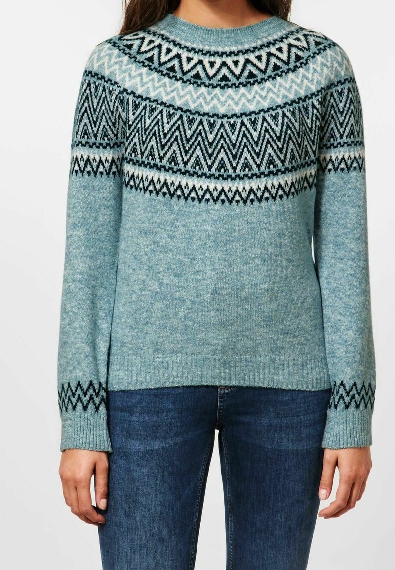 Pull bleu clair à col rond, avec un empiècement décoratif à motifs zigzag en noir, blanc et bleu foncé. Poignets et ourlet côtelés.