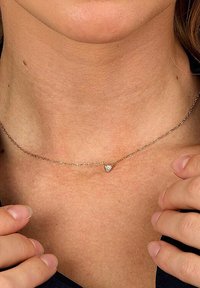 Goldfarbene Halskette mit feiner Kette und kleinem Herzanhänger, der eine subtile Textur aufweist. Um den Hals getragen, betont sie das Schlüsselbein.