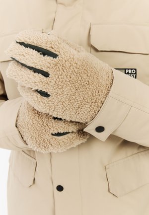 Beige, pluizige handschoenen met een gestructureerde buitenkant en groene accenten. Draagt over een lichtgekleurde jas met een knoopsluiting en patches.