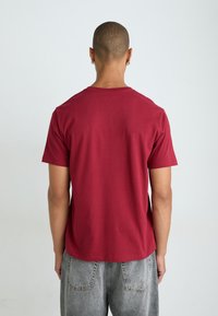 Μαρουλί μπλουζ�άκι φτιαγμένο από βαμβάκι, με κοντά μανίκια και στρογγυλή λαιμόκοψη, εμφανίζεται από το πίσω μέρος. Διαθέτει λεία υφή και άνετη εφαρμογή.