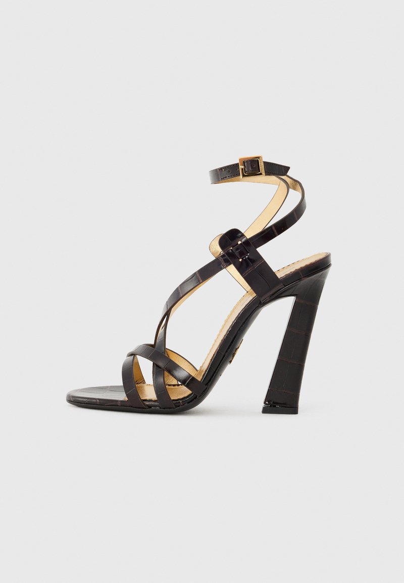 Black high-heeled sandals with crisscross straps, made from glossy material. Features a textured pattern and a gold buckle accent.