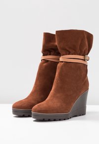 Bruna mocka kilstövlar med uppvikt topp, som har ett brunt läderrem runt ankeln och en texturerad svart gummisula.