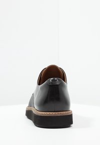 Chaussure en cuir noir avec panneaux latéraux texturés, talon arrondi et semelle extérieure en caoutchouc contrastante. Le design présente des coutures minimales et des accents subtils.