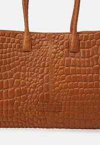 Hnědá kožená taška tote s krokodýlím vzorem, s dvojitými uchy, se středovým švem a logo nášivkou na dně.