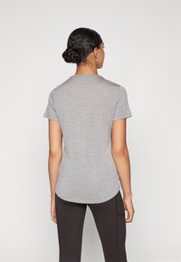 T-shirt cinza de manga curta com bainha arredondada, tecido leve, textura subtil e sem gráficos ou padrões visíveis. Usado com leggings escuras.