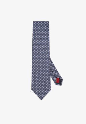Granatowy krawat z geometrycznym wzorem w jasnoniebieskim i białym kolorze. Wykonany z jedwabiu, z ostro zakończonym końcem i czerwoną metką z tyłu.