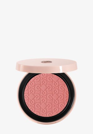 Poudre compacte dans un étui rose clair, avec un motif géométrique embossé sur la poudre corail-rose et un couvercle partiellement ouvert dévoilant un logo métallique.