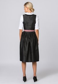 Schwarzes Kleid mit Blumenmuster, tailliertes Oberteil und voller Rock. Verfügt über einen pinken Taillengürtel, eine weiße Bluse mit Rüschenspiegel und schwarze Schuhe.