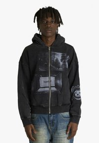 Felpa nera con zip e grafica frontale che raffigura alberi e una cornice con la parola "Recycund." Polsini e orlo a coste. Vestibilità casual.