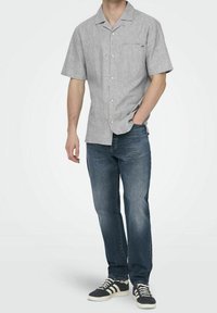 Ljusgrå kortärmad skjorta med knappar och ficka, matchad med mörkblå jeans och svarta sneakers med vita accenter.