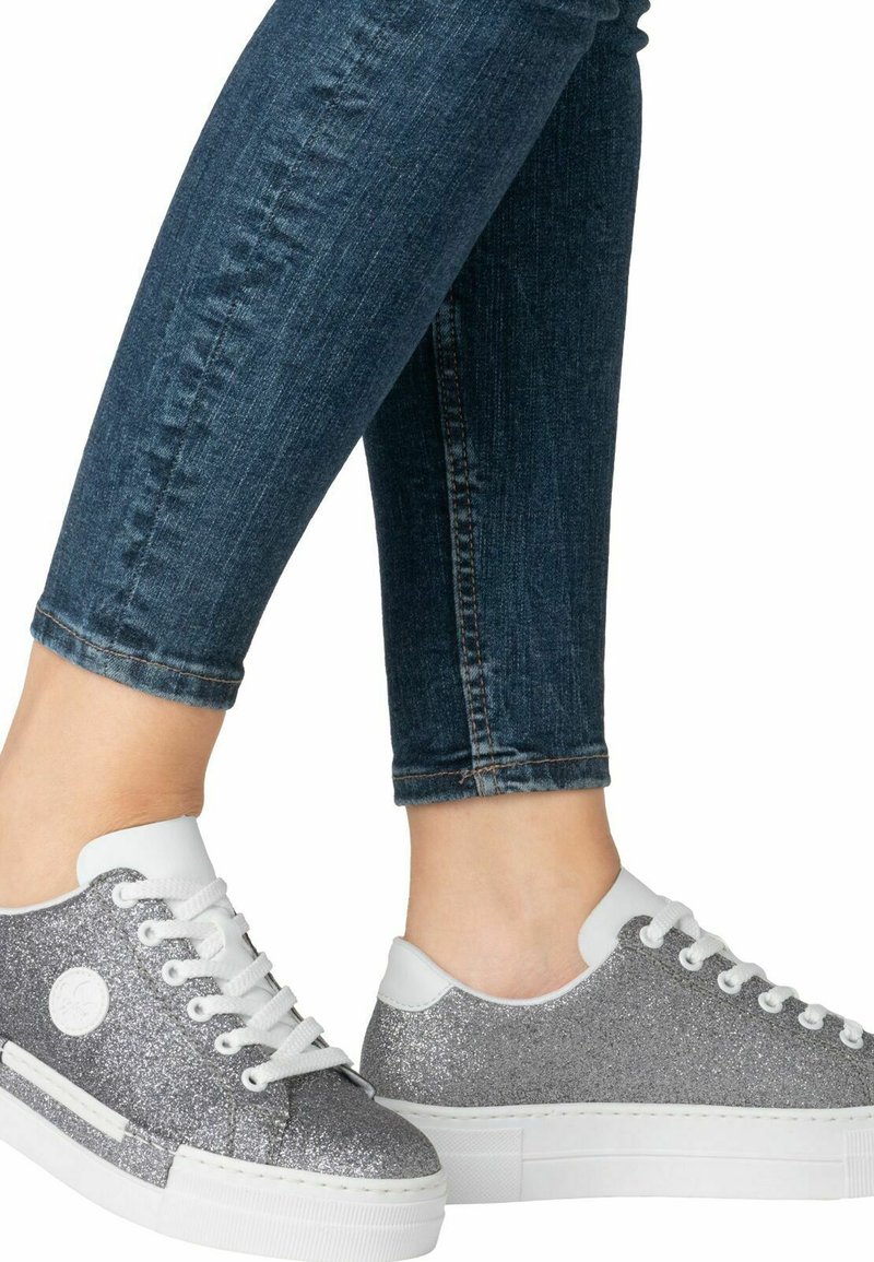 Baskets à paillettes argentées avec des accents blancs, bout rond et design à lacets. Associées à un jean bleu foncé bien ajusté qui met en valeur l'ourlet.