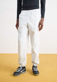 Pantaloni cargo albi, ușori, cu talie elastică și buzunare laterale, asortați cu pantofi sport alb-negru cu un design pattern.
