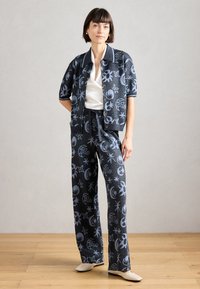 Ensemble coordonné bleu à motifs comprenant un haut à manches courtes avec boutons et un pantalon large, fabriqué à partir d'un tissu texturé orné de motifs célestes.
