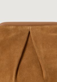 Cuscino in suede marrone con rifinitura in pelle liscia, caratterizzato da un design piegato distintivo e una texture morbida. Forma semplice ed elegante.