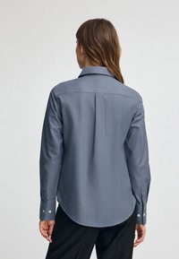 Camicia a maniche lunghe blu realizzata in tessuto liscio, con colletto classico, polsini con bottoni e orlo arrotondato sul retro.