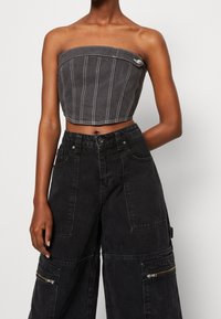 Trimmad grå denimtop med vertikala sömmar och en framficklåsdetalj. Matchas med löst sittande svarta cargobyxor med sidofickor.