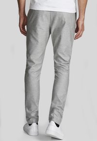 Pantalon gris clair fuselé en tissu texturé, avec un design épuré et une ceinture simple, assorti à des baskets blanches.