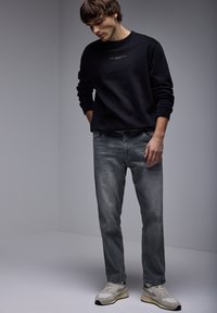Sudadera negra con cuello redondo, jeans gris deslavado, y zapatillas gris claro con un patrón texturizado y detalles en negro.
