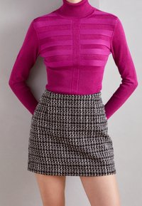 Haut en magenta ajusté avec un col roulé et des rayures horizontales, associé à une jupe mini à carreaux noir et blanc texturée, avec une finition en tissu lisse.