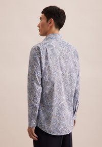 Koszula z długim rękawem w białym i niebieskim wzorze paisley, wykonana z lekkiego materiału. Posiada kołnierzyk zapinany na guziki oraz zaokrąglony dół.