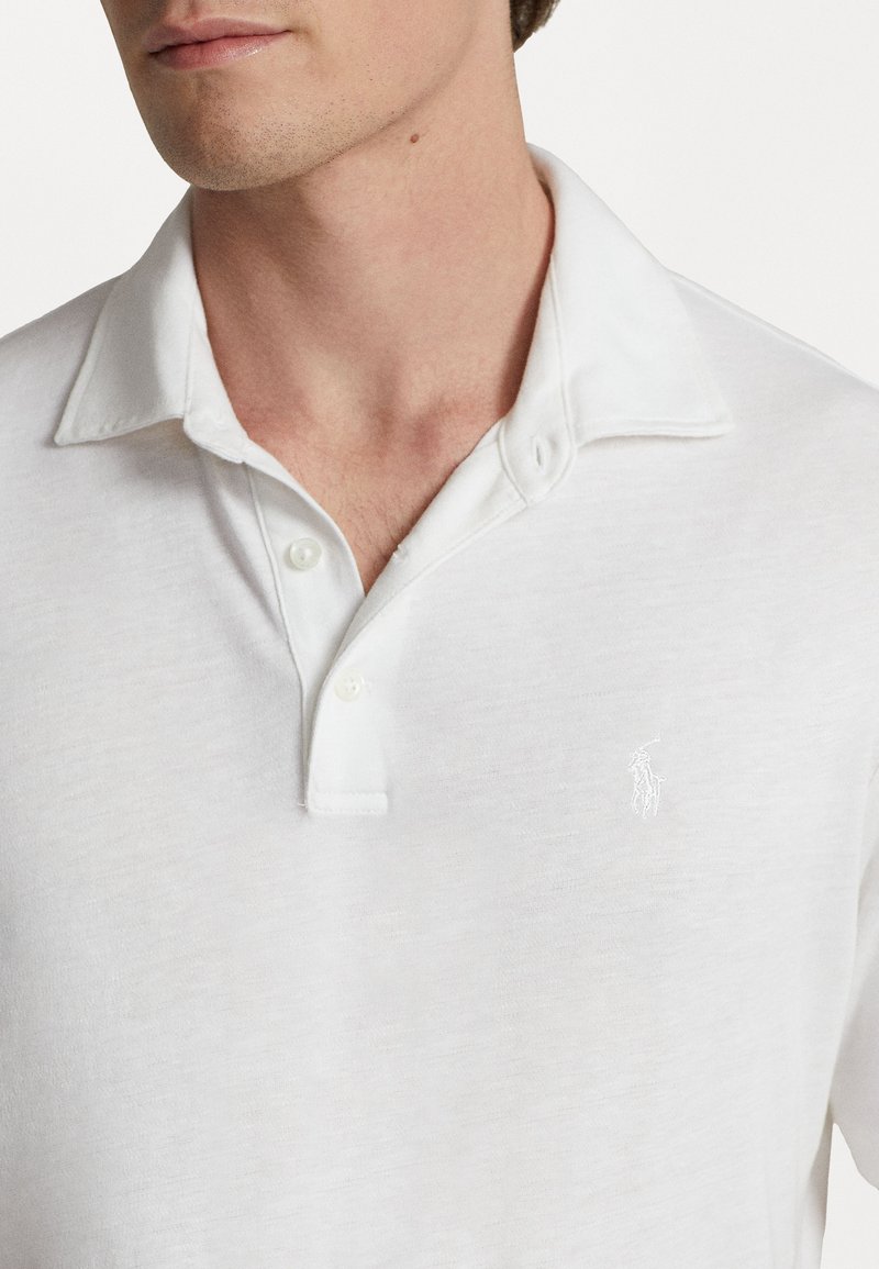Witte polo gemaakt van een gestructureerde katoenmix, met een kraag, twee knopen en een klein geborduurd logo op de borst.
