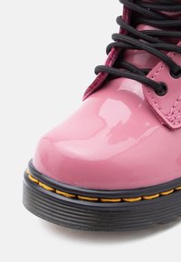 Λείος ροζ μποτάκι με μαύρα κορδόνια, μαύρη σόλα και κίτρινη λεπτομέρεια ραφής πάνω σε λευκό φόντο.