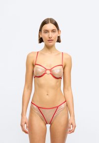 Σέτ εσωρούχων από διάφανο μπεζ υλικό με κόκκινες λεπτομέρειες. Περιλαμβάνει στηθόδεσμο με εσωτερικό στήριγμα και κεντρική λεπτομέρεια, καθώς και αντίστοιχο διάφανο σλιπ.