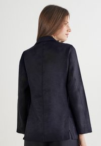 Ciemnoniebieska marynarka o gładkiej fakturze, z długimi rękawami i pojedynczym rozcięciem z tyłu. Posiada klasyczny kołnierz i dopasowany krój.