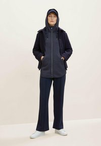 Granatowa polarowa kurtka z zamkiem, nałożona na ciemnoszary polarowy hoodie. Połączona z granatowymi spodniami o szerokich nogawkach i białymi trampkami.