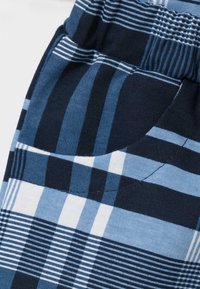 Niebieskie szorty w kratę z elastycznym paskiem w talii, z naprzemiennymi paskami granatowego, jasnoniebieskiego i białego koloru. Widoczna kieszeń.