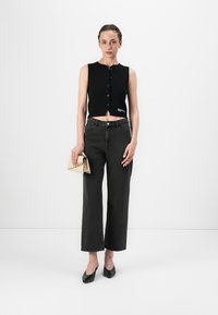 Black sleeveless knit top with front buttons, paired with high-waisted dark jeans, and a small tan handbag. Shoes are black heels.